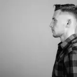 Perfil de hombre con un corte de pelo taper fade moderno y camisa a cuadros.