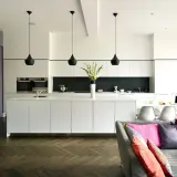 Modernt kök med en stor köksö och integrerade vitvaror. Svartvit inredning med detaljer i lila och färgglada kuddar i soffan.
