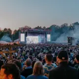 Stor publik vid Rosendal Garden Party. En stor scen med artister och ljusspel, omgiven av träd och tält.