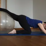Kobieta na macie ćwiczy z piłką, rozciągając nogę. Widać, co daje stretching: lepsza gibkość i relaks.
