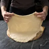 Ręce rozciągają elastyczne ciasto na pizzę, idealne do szybkiego przepisu na ciasto do pizzy.