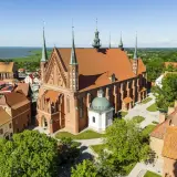 Zamek Frombork z lotu ptaka, z dominującą bazyliką katedralną i wieżami obronnymi, nad błękitną wodą Zalewu Wiślanego.