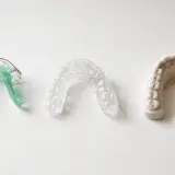 Tres dispositivos dentales: un retenedor verde, un retenedor transparente y un modelo de dientes con barra retenedora.