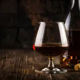 Kieliszek brandy i butelka na drewnianym stole. Idealny moment, by zastanowić się, z czym pić brandy.