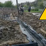 Budowa trwa: betonowanie ław fundamentowych. Pracownicy wylewają beton do wykopów z zbrojeniem.