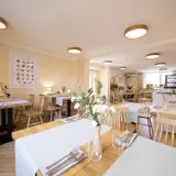 Przytulna restauracja z drewnianymi stołami i krzesłami, idealna na urodziny w łodzi dla dorosłych. Jasne ściany, subtelne oświetlenie i świeże kwiaty tworzą miłą atmosferę.