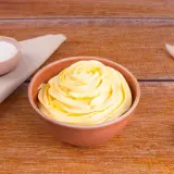 Una ciotola piena di soffice crema al burro, pronta per decorare torte. Accanto, ciotoline con zucchero e decorazioni naturali.