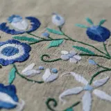 Un fichier broderie aux motifs floraux bleus et blancs sur fond beige. Les détails des points de couture sont visibles.