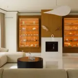 Nowoczesny salon z kominkiem, przeszklonymi witrynami i beżową sofą.