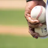 Dłoń trzyma dwie piłki baseballowe, gotowe do gry. Widać napis "EXTRA INNINGS TECHNOLOGY", świadczący o zaawansowanej technice niskiej piłki.