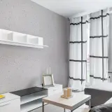 Nowoczesny salon z szarą ścianą pokrytą tynkiem japońskim o subtelnych wzorach. Białe meble i zasłony w kratę dodają lekkości.