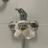 Kran prysznicowy owinięty folią, bo w bloku brak ciepłej wody. Krople zimnej wody spływają po opakowaniu.