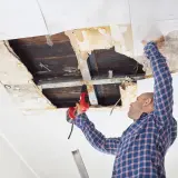 Mann repariert Decke nach kleinem Wasserschaden. Trocknung und Reparatur sind im Gange.