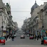 Ulica Piotrkowska w Łodzi, pełna zabytkowych kamienic, latarni i ruchu ulicznego. Dwa czerwone pojazdy z napisem "Miejsce na reklamę" stoją przy chodniku.