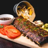 Délicieux ribs de porc, parfaitement cuits, accompagnés de frites, tomates et cornichons. Un festin pour les amateurs de cuisson ribs.