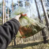 Ręka trzyma worek ze śmieciami w lesie. Zasady "leave no trace" to dbanie o przyrodę.