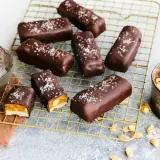 Vegane Snickers mit Karamell, Erdnüssen und Meersalz bestreut, auf einem goldenen Gitter.