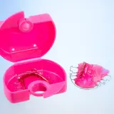 Caja ortodoncia rosa abierta con un retenedor dentro y otro fuera.