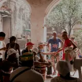 Ludzie w Guantanamera, w tym mężczyzna w czerwonym stroju i kapeluszu, ściskają sobie dłonie.