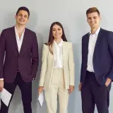 Trzy uśmiechnięte osoby w eleganckich strojach. Idealny przykład, co ubrać na rozmowę kwalifikacyjną.