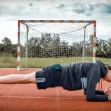 Mann in Unterarmstütz, um den Rumpf zu stabilisieren, vor einem Fußballtor.