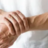 Mężczyzna trzyma się za lewą rękę, odczuwając ból od łokcia do dłoni.