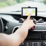 Dłoń dotyka ekranu nawigacji samochodowej, która pokazuje mapę. To najlepsza nawigacja samochodowa na telefon, która ułatwia podróż.