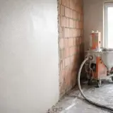 Maszyna do tynkowania ścian pracuje, nanosząc równomierną warstwę tynku na ceglaną ścianę.