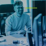 Un homme souriant travaille sur son application bureau, entouré d'écrans d'ordinateur dans un espace moderne.