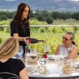 Degustazione di vino alla Baldetti Winery: una giovane donna versa vino rosso in un bicchiere, mentre gli ospiti assaporano il paesaggio.