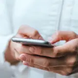 Dłonie trzymające smartfon, uważaj na oszustwa typu smishing, które mogą przyjść w każdej chwili.