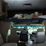 Un homme dort dans un camping-car 4 places. Une unité de climatisation portable et une station d'énergie sont visibles.