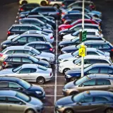 Rząd samochodów na parkingu. Znak "Kasse" sugeruje, że to parking płatny. KNF co to? To może być skrót od nazwy firmy zarządzającej parkingiem.