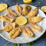 Bocartes fritos crujientes y dorados, servidos en un plato con rodajas de limón y perejil fresco. ¡Un manjar listo para disfrutar!