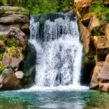 Wodospad w skalistej scenerii, idealny cel dla miłośników **best waterfall hikes**. Zielona woda i bujna roślinność.