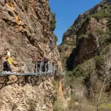 Gente camina por las pasarelas de Alquézar, un sendero suspendido entre imponentes paredes rocosas y vegetación.
