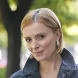 Portret Haliny Młynkowej z krótkimi blond włosami, w kurtce, na tle drzew.