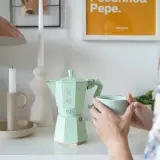 Miętowa kawiarka Bialetti, czy stalowa czy aluminiowa, idealna na poranną kawę. Obok świeca i kubek.