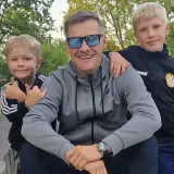 Marcin Mroczek z uśmiechem i dwoma synami, którzy przytulają się do niego.