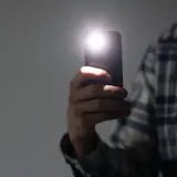 Dłoń trzyma telefon, którego latarka w telefonie rozświetla ciemność.