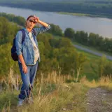 Donna in gravidanza, con zaino, su un sentiero di montagna a 1500 metri, con vista sul fiume.