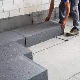 Pracownik układa szary styropian pod wylewkę, tworząc izolację podłogi.