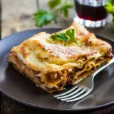 Pyszny kawałek lasagne z mięsem mielonym, idealny na prosty obiad. Posypana parmezanem i udekorowana natką pietruszki.