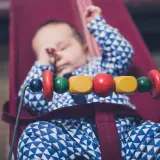 Sover gott i sin babysitter elektrisk, med färgglada träpärlor som leksak.