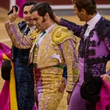 Tres toreros con trajes de luces, uno con coleta de torero, son felicitados en la arena.