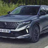 Nowy Austral Renault pędzi po drodze, otoczony zielenią.