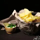 Koszyk pełen chipsów tortilla, obok miseczka z dipem i ziołami. Czy chipsy tortilla są zdrowe? To zależy od składników i sposobu przygotowania.