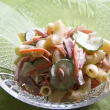 A close-up of a crystal bowl filled with creamy Japanese macaroni salad, featuring elbow macaroni, shredded carrots, sliced cucumbers, and ham.