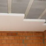 Ocieplenie stropu styropianem w trakcie budowy. Widoczne betonowe pustaki stropowe, płyty styropianowe i ściana z cegły.