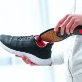 Une personne insère une semelle intérieure dans une chaussure. La semelle intérieure, avec sa texture naturelle, illustre la définition d'une semelle élastomère.